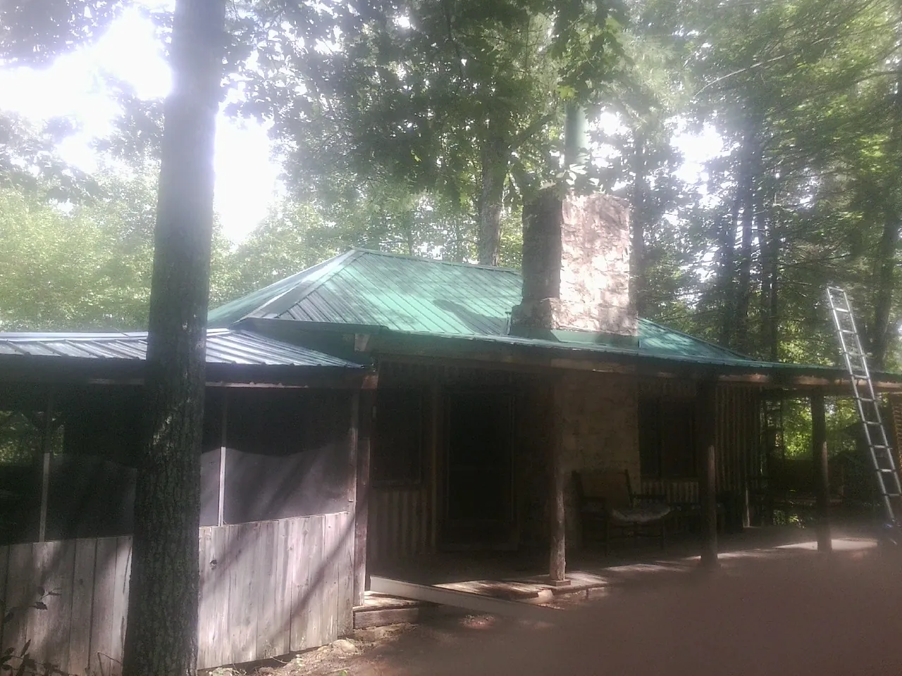 Green metal roof and stone chimney above a log cabin porch in Pineville