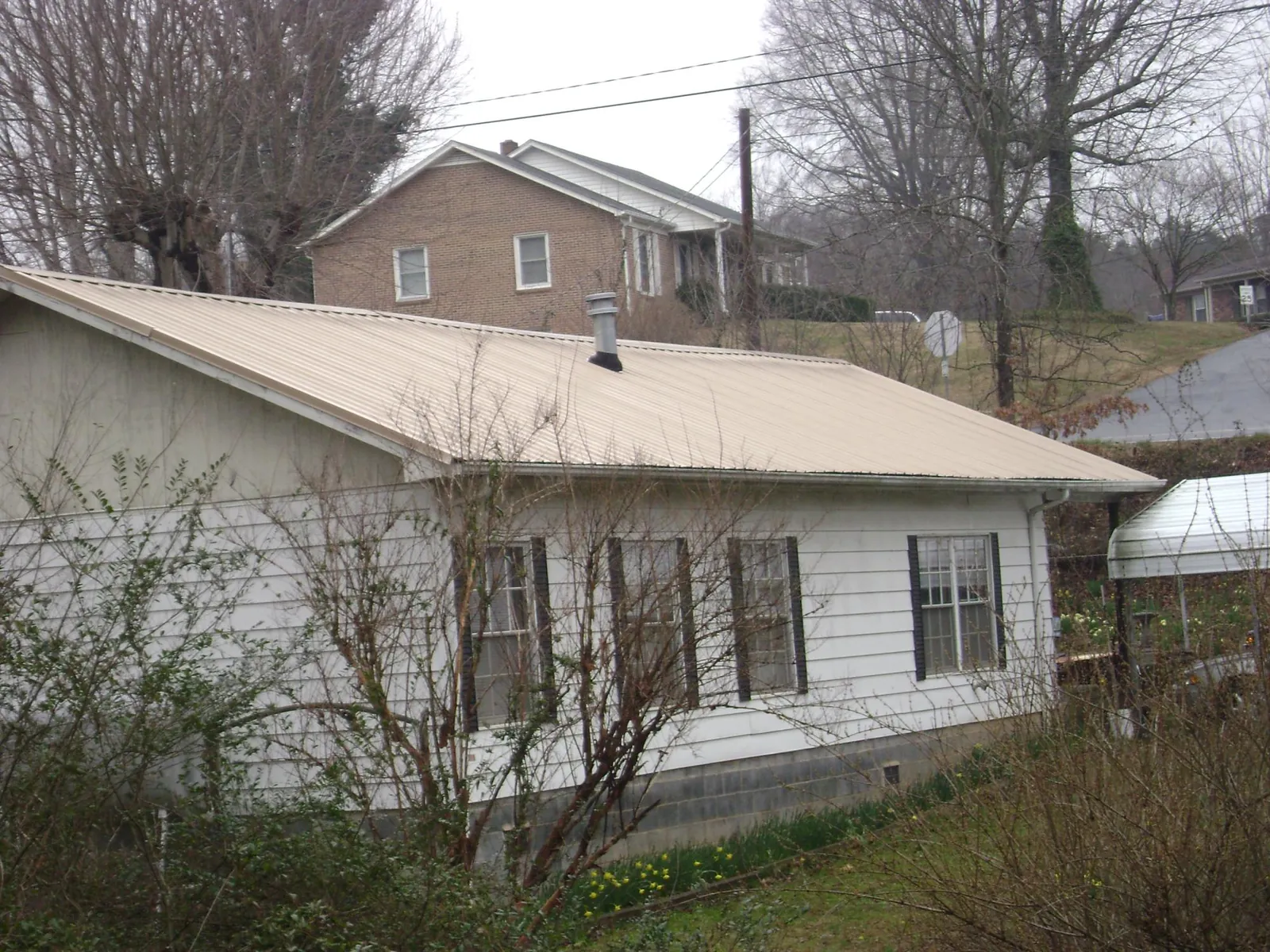 Tan metal roof on a white sided house set into a hillside — Commercial Roofing by Roofing Brothers in Pineville